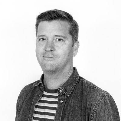 Råger Mårlind i svartvitt porträtt visar leende och denimskjorta.