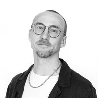 Rasmus Lehnér i svartvitt porträtt med glasögon och halsband.