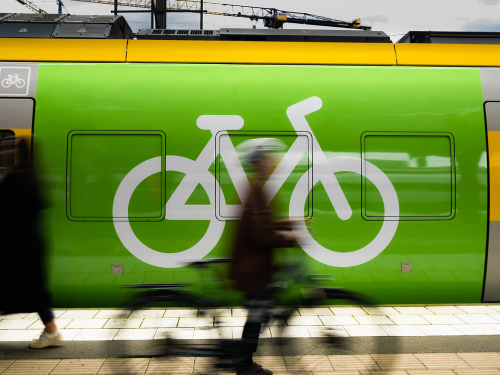Visar grönt tåg med cykelsymbol, suddiga personer passerar.