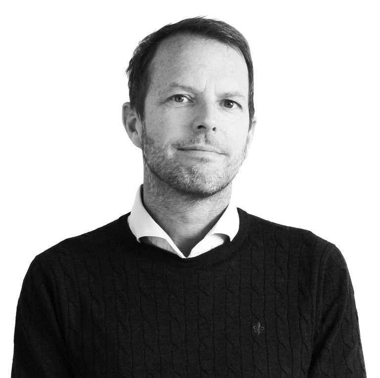 Mikael Ene i svartvitt porträtt. Ser rakt fram. Bär tröja.