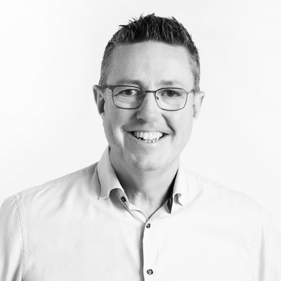 Thomas Svahn i svartvitt porträtt ler och bär glasögon.